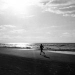日の光のあたる海辺を走る写真